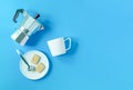 On a blue background aluminum geyser coffee maker and white porcelain cup and saucer with cookies