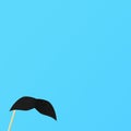 Blue background with fake black mustache on a stick Royalty Free Stock Photo