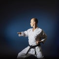 On a blue background with a gradient, an athlete with a black belt trains formally karate exercises.