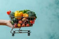 Blue background, hand holds shopping cart filled with fruits and vegetables Royalty Free Stock Photo