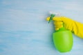 On a blue background, a hand in a yellow glove holds a green bottle for spraying liquids, there is a place for writing on the left Royalty Free Stock Photo