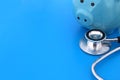 On a blue background lies a stethoscope and a piggy bank.