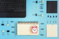 On a blue background neatly spread out clerical clips and clothespins. In the corner is a black laptop. On the open page