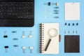 On a blue background neatly spread out clerical clips and clothespins. In the corner is a black laptop. On the open page