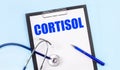 On a blue background, a stethoscope, a pen and a tablet with paper and the text CORTISOL. Medical concept