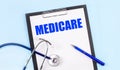 On a blue background, a stethoscope, a pen and a tablet with paper and the text MEDICARE. Medical concept