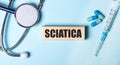 On a blue background, a stethoscope, a syringe and pills and a wooden block with the word SCIATICA. Medical concept