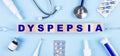 On a blue background, a stethoscope, a thermometer, other medicines and wooden cubes with the text DYSPEPSIA. View from above.