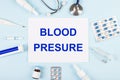 On a blue background, a stethoscope, a thermometer, pills, medicine bottles and a piece of paper with the text BLOOD PRESURE