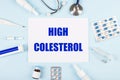 On a blue background, a stethoscope, a thermometer, pills, medicine bottles and a piece of paper with the text HIGH COLESTEROL Royalty Free Stock Photo