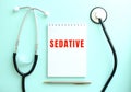 On a blue background, a stethoscope and a white notepad with the words SEDATIVE. Royalty Free Stock Photo
