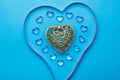 On a blue background, there is a heart made of transparent pebbles in the shape of hearts in the middle, a gold heart and a ribbon Royalty Free Stock Photo