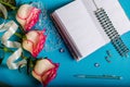 On a blue background there are three roses, opened empty notebook, pen Royalty Free Stock Photo