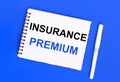 On a blue background, a white ballpoint pen and a white notepad with the text INSURANCE PREMIUM. View from above Royalty Free Stock Photo