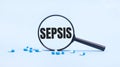 On a blue background, white and blue capsules with pills and a black magnifying glass with the text SEPSIS. Medical concept