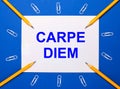 On a blue background, white paper clips, yellow pencils and a white sheet of paper with the text CARPE DIEM Royalty Free Stock Photo