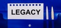 On a blue background, white pens and a sheet of paper with the text LEGACY Royalty Free Stock Photo
