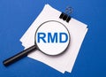 On a blue background, white sheets under a black paper clip and on them a magnifying glass with the text RMD Required Minimum Royalty Free Stock Photo