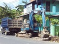 Blue backhoe on the street and blue dump truck