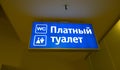 Blue backlit sign. Public WC. Text Translation from Russian: Paid toilet.