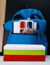 Blue backpack with colored pencils and paints on a black background and next to the book Royalty Free Stock Photo