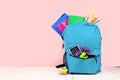 Blue backpack full of school supplies against a pink background. Back to school.