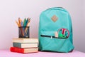 Blue backpack and school supplies: notepad, books, scissors, pens, pencils, ruler, calculator is on pink wooden table