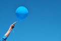 Blue balloon on a background of blue sky. Girl`s hand holding ball on white rope, close-up with copy space