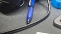 A blue ballpoint pen resting on a textured black surface, surrounded by a black cable, showcasing a typical workstation Royalty Free Stock Photo