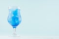 Blue beach cold alcohol drink with curacao liquor, ice cubes in elegant wineglass on pastel blue background and white wood table.