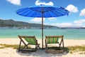 A blue beach umbrella and striped chaise lounges Royalty Free Stock Photo