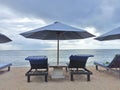 Blue beach umbrella with wooden deck chairs. Relax on vacation background concept with calm beach view and the sky clouds. Royalty Free Stock Photo