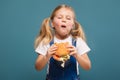 Adorable cute little girl in white shirt and jean jumpsuit with hamburger Royalty Free Stock Photo