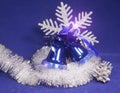 Blue beautiful New Year`s ornament - a hand bell with a bow, brilliant tinsel, silver cones and a snowflake on a blue background Royalty Free Stock Photo