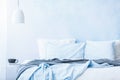 Blue bedsheets and pillows on bed next to a table with a cup under white lamp in simple bedroom interior Royalty Free Stock Photo