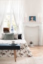 Green bench in front of patterned bed with pillows in white bedroom interior with poster. Real photo