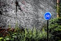 Blue Bicycle Sign Against Greenery and Brick Wall