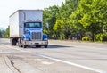 Blue big rig day cab semi truck for local delivery transporting cargo in semi trailer running on wide street with green trees Royalty Free Stock Photo