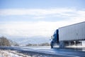 Blue big rig long haul semi truck transporting cargo in refrigerated semi trailer running on wet winter road with melting snow Royalty Free Stock Photo