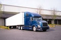 Dark blue big rig semi truck with trailer in warehouse dock load Royalty Free Stock Photo