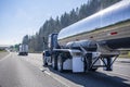 Blue big rig semi truck with shiny tank semi trailer driving on the wide highway road behind another truck Royalty Free Stock Photo