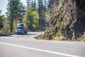 Blue big rig semi truck transporting cargo in covered bulk semi trailer turning around the cliff on the winding road with autumn Royalty Free Stock Photo