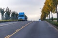 Blue big rig semi truck transporting on the flat bed semi trailer oversized load driving downhill on the autumn empty road
