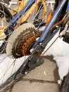 Blue bike has been outside all winter and got broken. Rusty bicycle chain hangs on sprocket and gear.