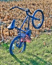 A blue bike leaning backward by itself with a flag in the spokes in a field