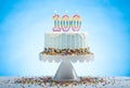 Blue Birthday Cake with Sprinkles on a White Cake Plate and Blue Background with 100 candles on Top