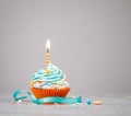 Blue Birthday Cupcake with orange Candle over grey Royalty Free Stock Photo