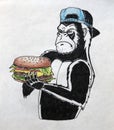 Gorilla in a blue cap holds a burger in its paws