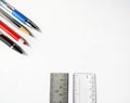 Blue black and red pens a pencil a metal scale and a plastic scale on an isolated white background