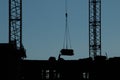 Blue-Black Silhouette of Worker in Hard Hat directing Cargo on Construction Site surrounded by Construction Machinery Royalty Free Stock Photo